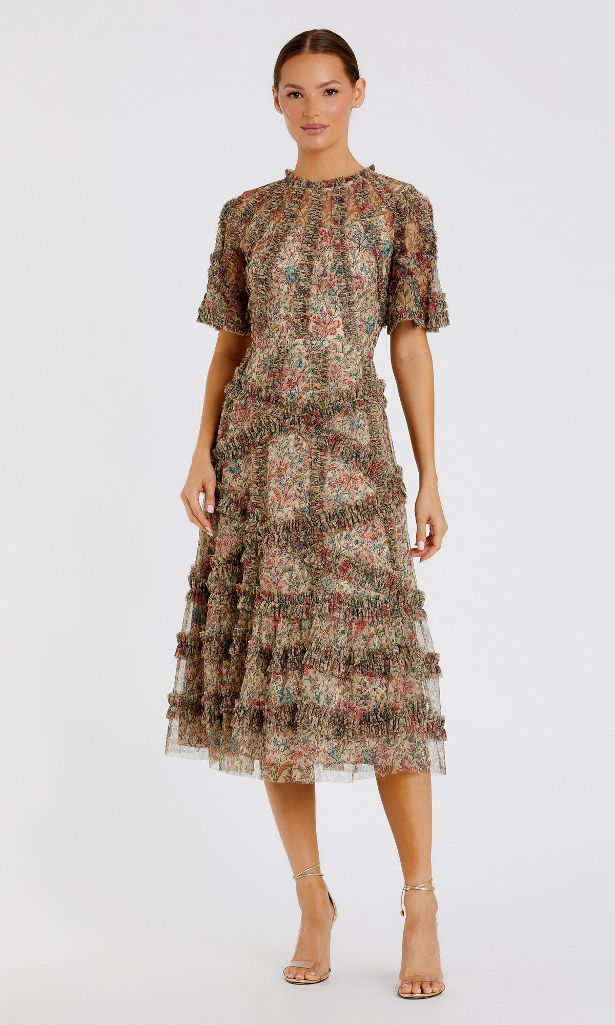 A woman wears the Mac Duggal 8010 short-sleeve wedding-guest dress in beige multi, featuring a floral print and tiered ruffles. Her hair is pulled back, and she completes the look with strappy nude heels.